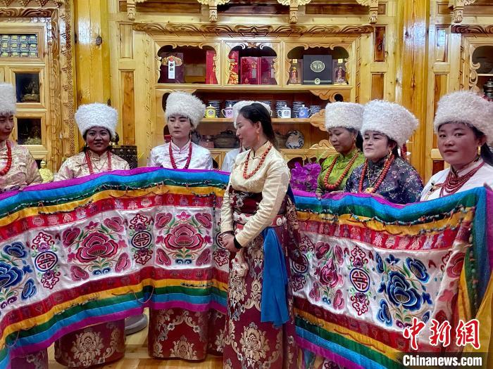 圖為女性展示村民自發(fā)繡制的“百米五彩哈達(dá)”。　李玉峰 攝